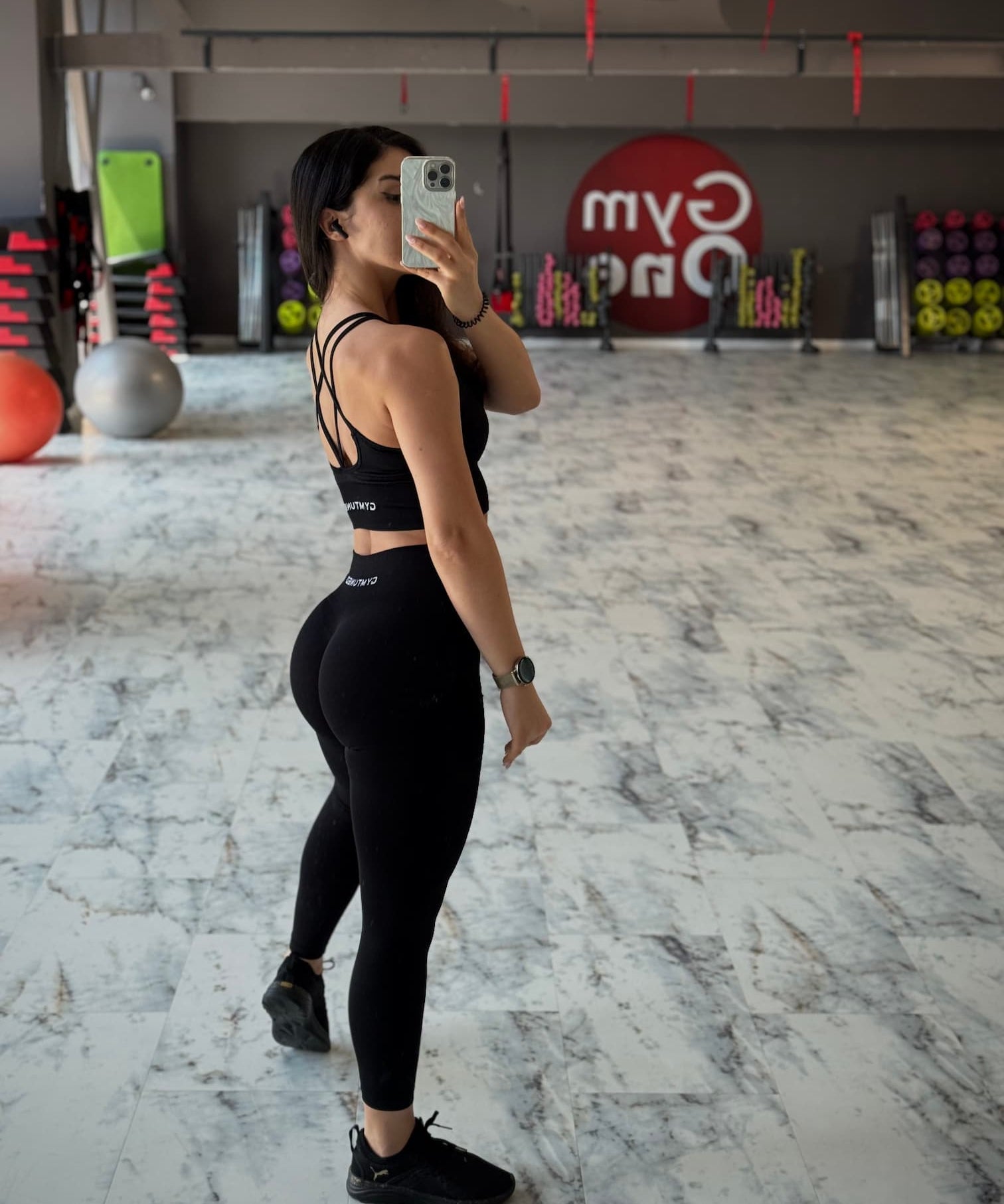 Set sport GYMTUNED negru – bustieră cu bretele încrucișate și colanți modelatori, poză laterală în sală de fitness