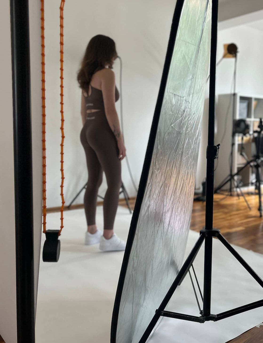 Backstage la ședința foto GYMTUNED – model purtând colanți modelatori și bustieră sport maro, fotografiată în studio printre echipamentele de producție.