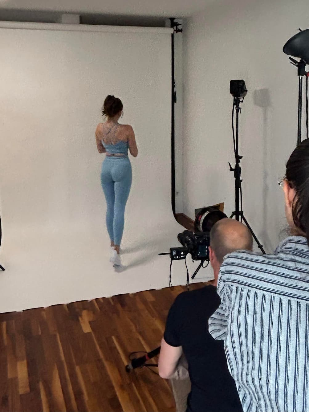 Ședință foto GYMTUNED în studio – model purtând colanți modelatori și bustieră sport albastru pastel, surprinsă din unghiul echipei de producție.