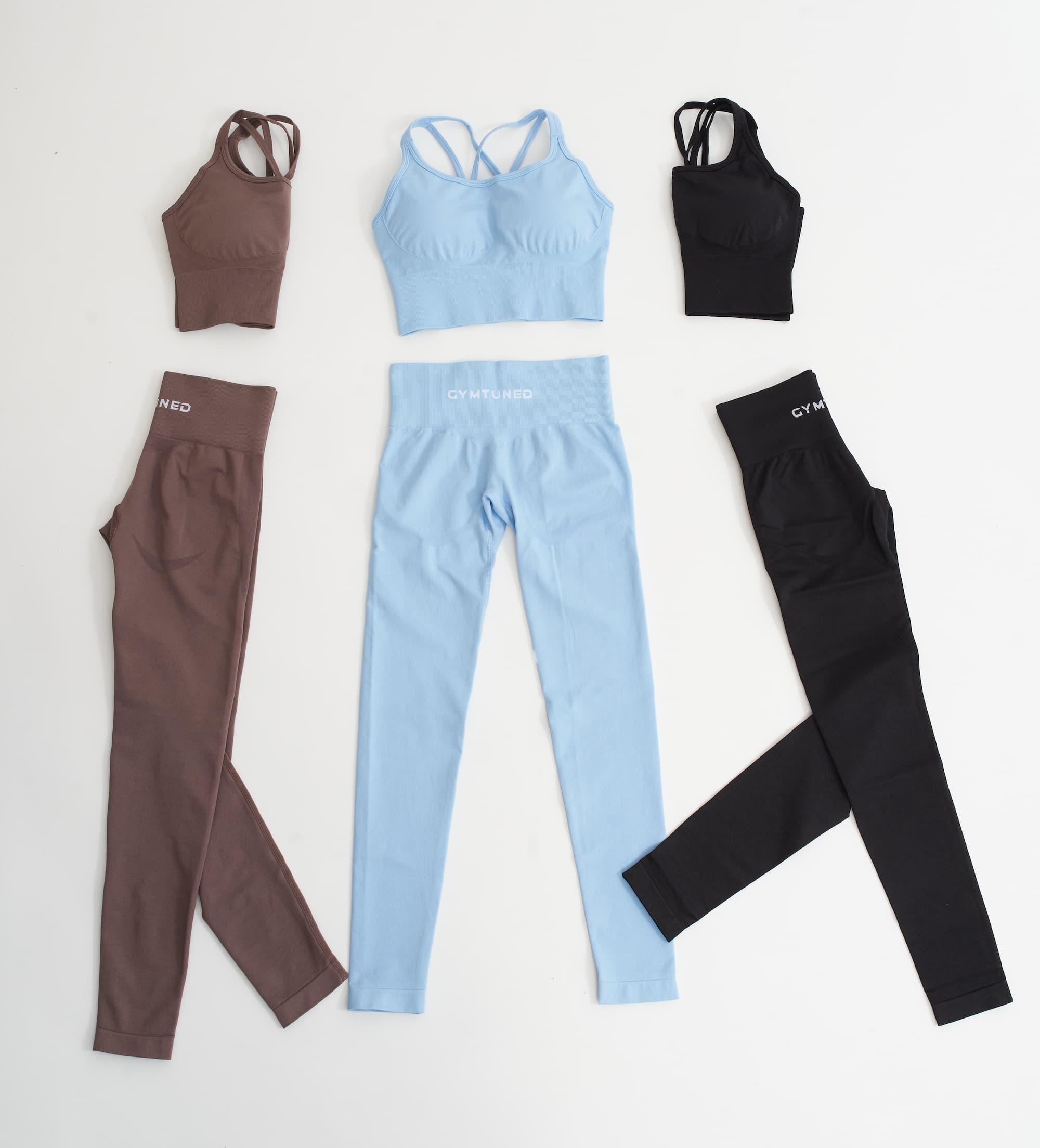 Seturi GYMTUNED formate din colanți modelatori și bustiere sport – în culorile maro, negru și albastru pastel, fotografiate flat lay pentru sală și fitness.