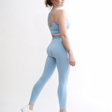 Set Original by Gymtuned în albastru pastel – vedere din spate cu bustieră sport pentru fitness si sala cu bretele încrucișate și colanți modelatori seamless, purtate de model